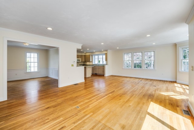 unfurnished living room with visible vents, light wood-style flooring, crown molding, and a wealth of natural light