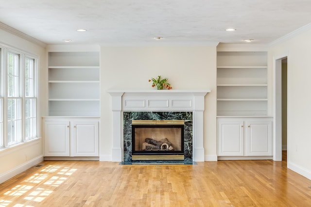 unfurnished living room featuring ornamental molding, light wood finished floors, and built in shelves
