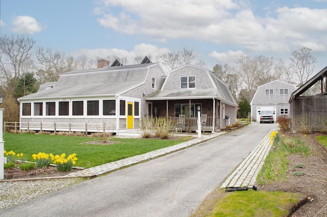 view of front of property featuring covered porch, a sunroom, a garage, a front lawn, and an outdoor structure