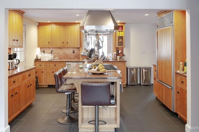 kitchen featuring dark tile patterned floors, island range hood, a kitchen island, paneled fridge, and a breakfast bar area