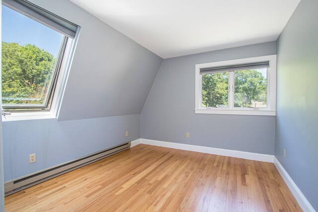 additional living space featuring light wood-type flooring, vaulted ceiling, and a baseboard radiator