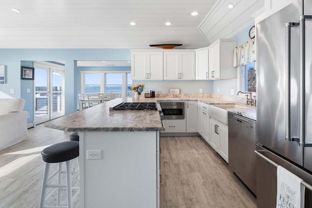 kitchen featuring white cabinets, appliances with stainless steel finishes, open floor plan, light wood-style floors, and a kitchen bar