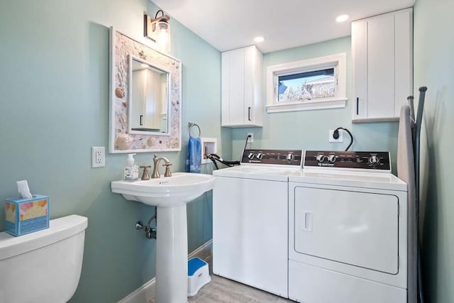 clothes washing area with washing machine and dryer, laundry area, a sink, baseboards, and light wood finished floors