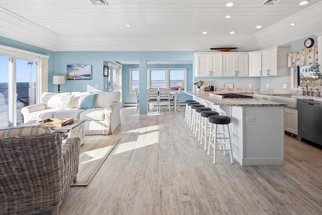 kitchen featuring dishwasher, a breakfast bar area, light stone countertops, light wood-type flooring, and white cabinetry