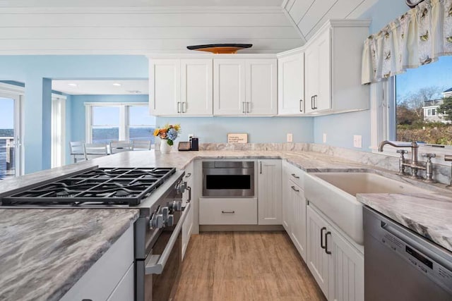 kitchen with light stone counters, stainless steel appliances, white cabinets, a sink, and light wood-type flooring