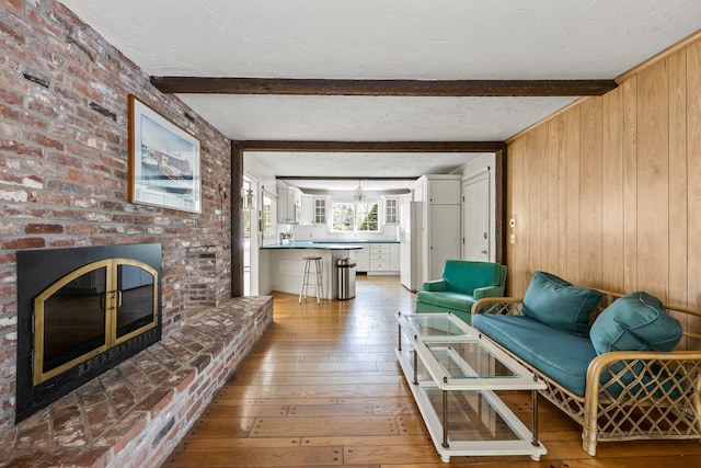 154 Cotuit Bay Dr, Cotuit, MA 02635 - living room with wooden walls, beam ceiling, wood-type flooring, a brick fireplace, and a textured ceiling