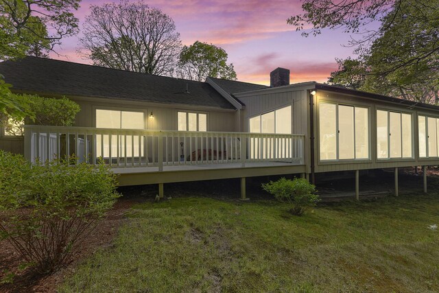 154 Cotuit Bay Dr, Cotuit, MA 02635 - back of house at dusk with a chimney, a wooden deck, a lawn, and a sunroom