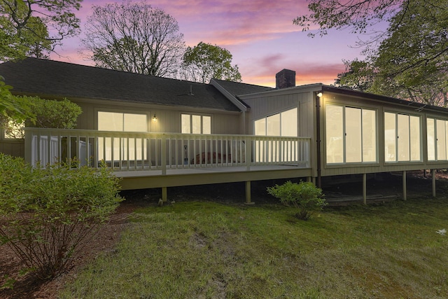 154 Cotuit Bay Dr, Cotuit, MA 02635 - back of house at dusk with a chimney, a wooden deck, a lawn, and a sunroom