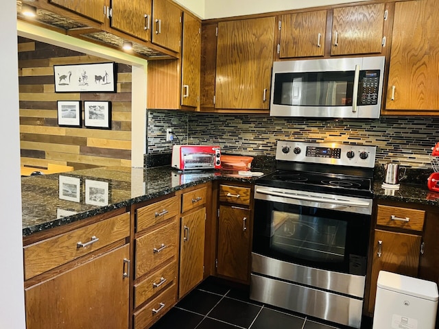 kitchen with decorative backsplash, dark tile patterned flooring, appliances with stainless steel finishes, and dark stone counters