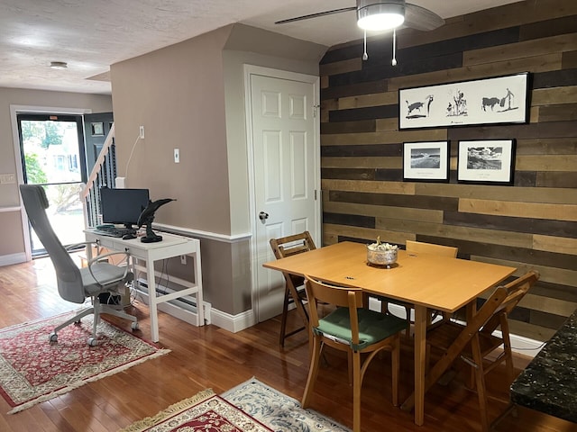 dining room with hardwood / wood-style floors, wooden walls, and ceiling fan