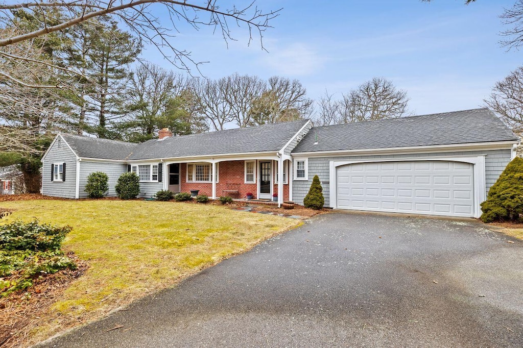 single story home with driveway, a chimney, an attached garage, a front yard, and brick siding