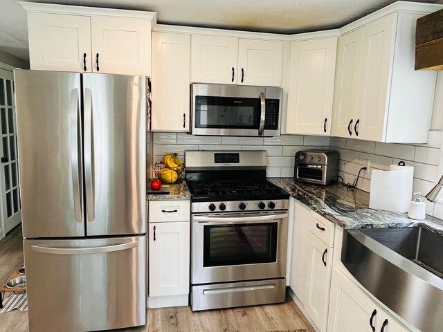 19 Artisan Way, Forestdale, MA 02644 - kitchen featuring appliances with stainless steel finishes, dark stone countertops, backsplash, white cabinets, and light wood-type flooring