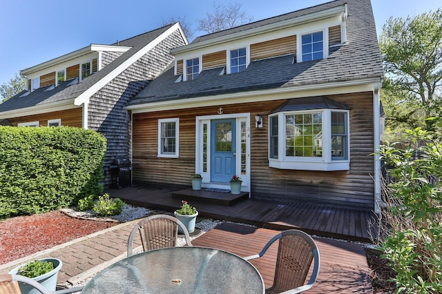 view of front of house with outdoor dining area, a deck, and roof with shingles