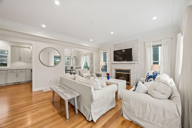 living area featuring crown molding, recessed lighting, light wood-style flooring, a large fireplace, and baseboards