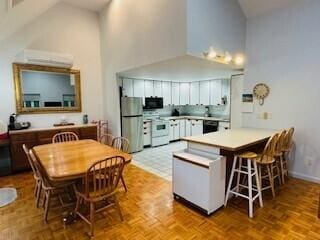 kitchen with light parquet floors, high vaulted ceiling, kitchen peninsula, white range, and stainless steel fridge