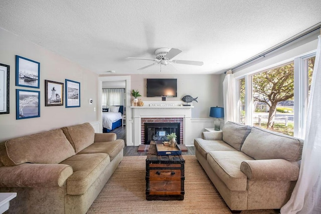 living area with a textured ceiling, ceiling fan, wainscoting, and a fireplace