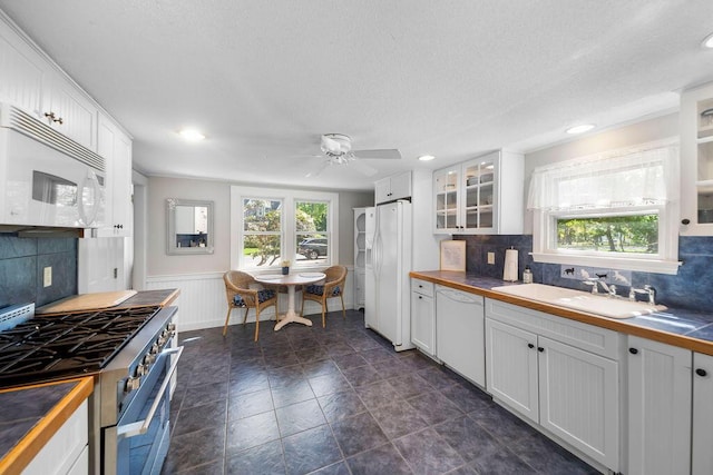 kitchen with white appliances, a sink, white cabinetry, glass insert cabinets, and a wainscoted wall