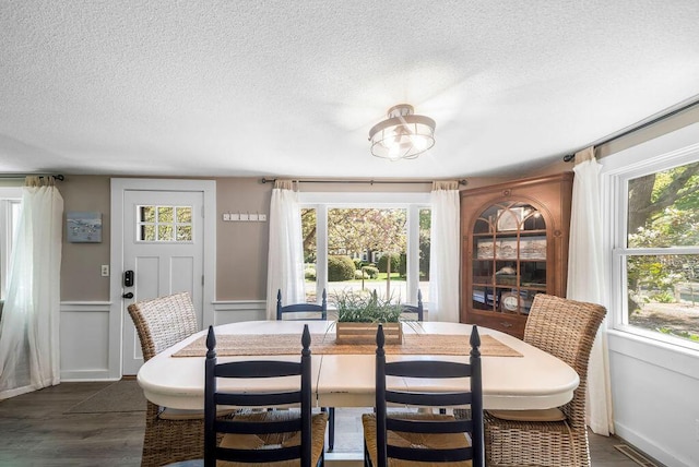 dining area featuring a textured ceiling, dark wood-style flooring, a wainscoted wall, and a decorative wall