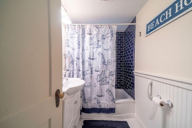 bathroom featuring shower / bathtub combination with curtain, a wainscoted wall, a textured ceiling, and vanity
