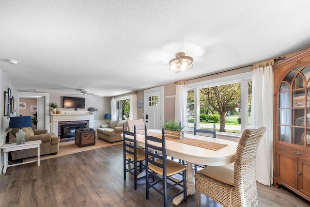 dining room with a textured ceiling, a ceiling fan, wood finished floors, and a brick fireplace