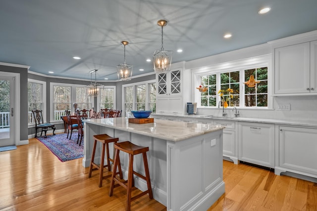 kitchen with light stone counters, hanging light fixtures, a center island, and white cabinets