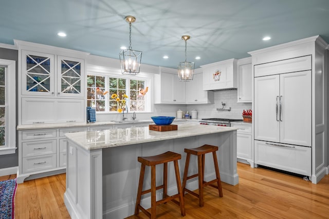 kitchen featuring white cabinetry, a center island, hanging light fixtures, light hardwood / wood-style flooring, and paneled refrigerator