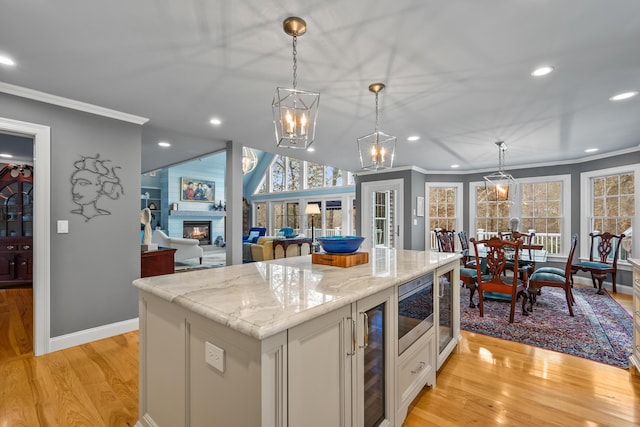 kitchen featuring decorative light fixtures, white cabinetry, ornamental molding, a center island, and light stone counters