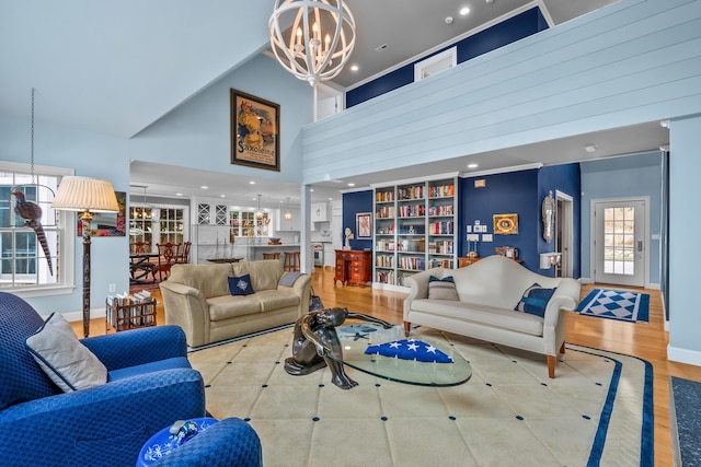 living room featuring a high ceiling, built in shelves, a chandelier, and light wood-type flooring