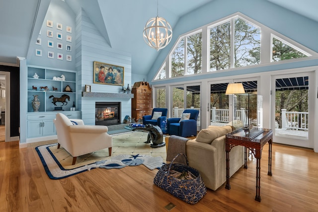 living room with a healthy amount of sunlight, a chandelier, high vaulted ceiling, and light hardwood / wood-style flooring