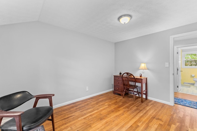 office area with light wood-type flooring, vaulted ceiling, and a textured ceiling