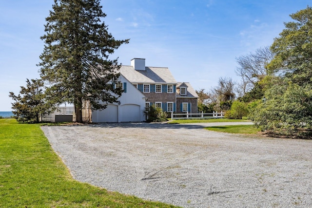 view of front of house featuring a chimney, driveway, a front lawn, and an attached garage