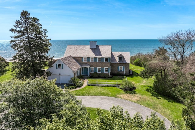 view of front of home with a water view, a front lawn, a chimney, and driveway