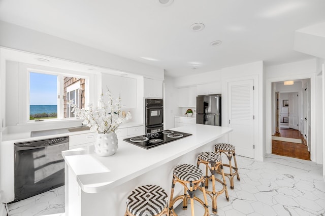 kitchen featuring marble finish floor, a kitchen bar, white cabinetry, black appliances, and light countertops