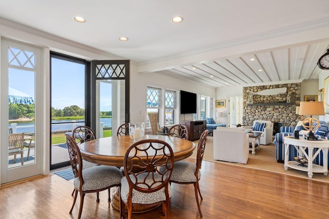 dining space featuring a water view, beam ceiling, light hardwood / wood-style floors, and a fireplace