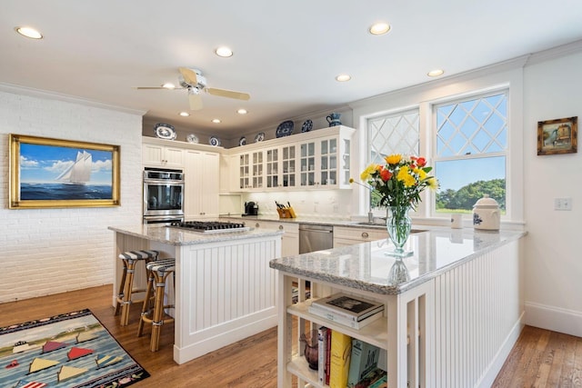 kitchen with light wood-type flooring, light stone countertops, brick wall, a kitchen island, and a breakfast bar area