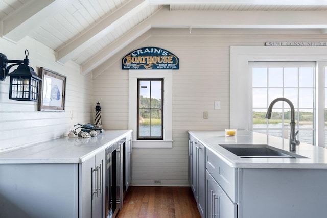 kitchen with dark wood-type flooring, vaulted ceiling with beams, sink, gray cabinets, and wood walls