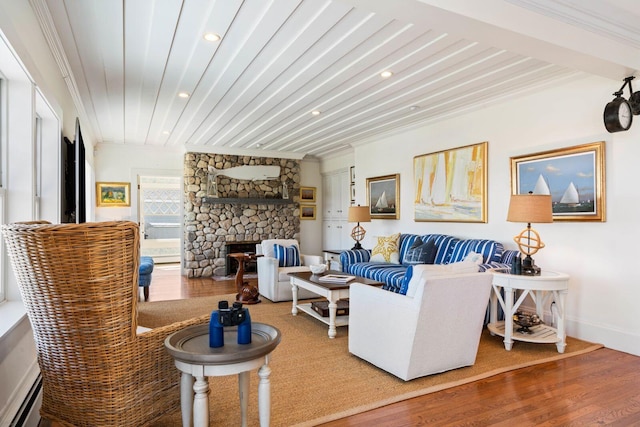 living room featuring hardwood / wood-style flooring, a baseboard heating unit, ornamental molding, and a stone fireplace