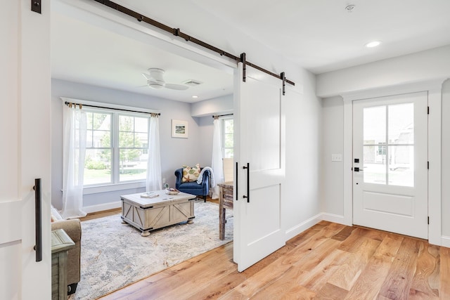 foyer with light hardwood / wood-style flooring, ceiling fan, and a barn door