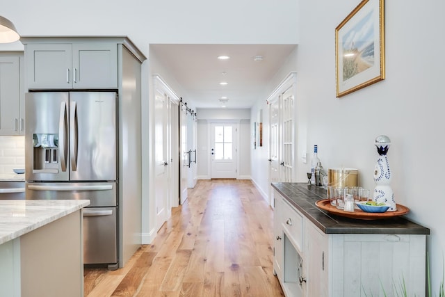 kitchen with light stone countertops, light hardwood / wood-style floors, stainless steel fridge, a barn door, and gray cabinets