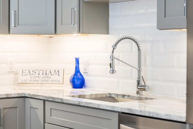 interior details with dishwasher, sink, backsplash, gray cabinetry, and light stone counters