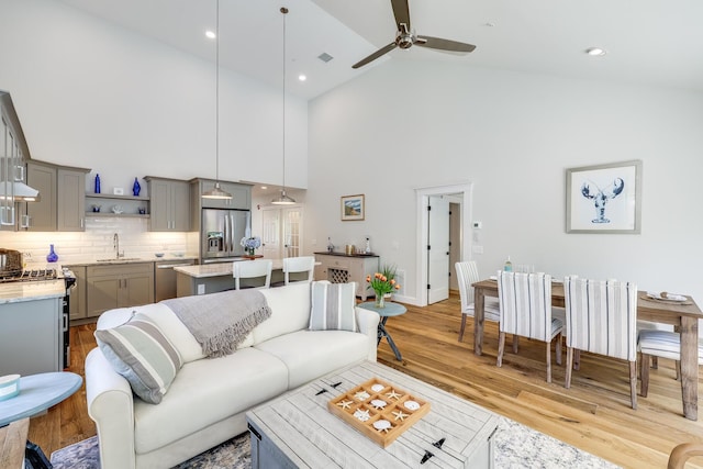 living room featuring high vaulted ceiling, sink, light hardwood / wood-style flooring, and ceiling fan