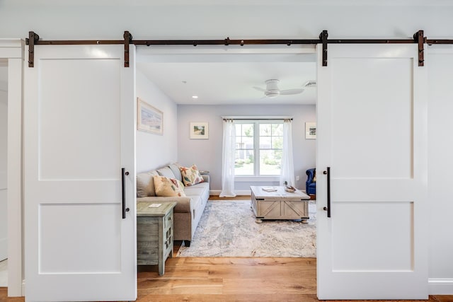 interior space with ceiling fan, a barn door, and light wood-type flooring