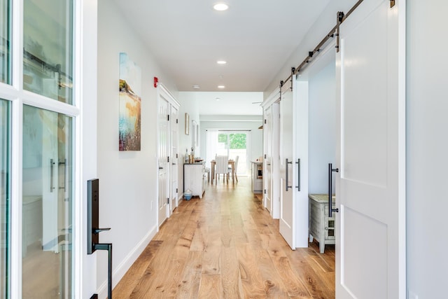 hall with light wood-type flooring and a barn door