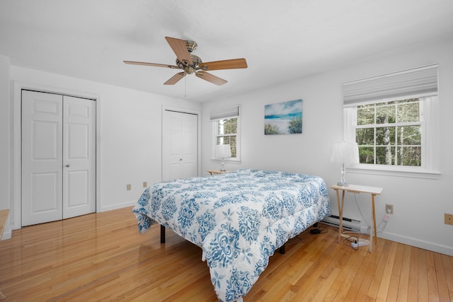 bedroom with a baseboard radiator, ceiling fan, baseboards, light wood finished floors, and multiple closets