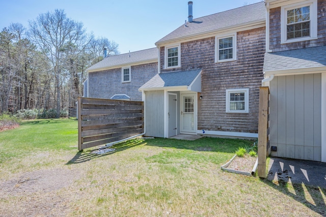 exterior space featuring a lawn, fence, and a shingled roof