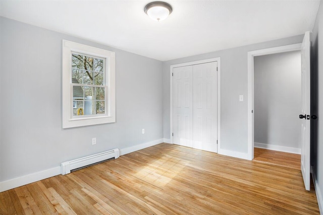 unfurnished bedroom featuring baseboard heating, wood-type flooring, and a closet