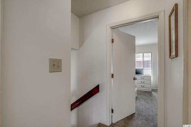 corridor featuring dark colored carpet and a textured ceiling