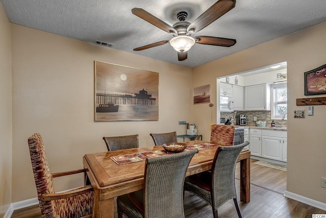 dining room with light hardwood / wood-style floors, ceiling fan, and a textured ceiling