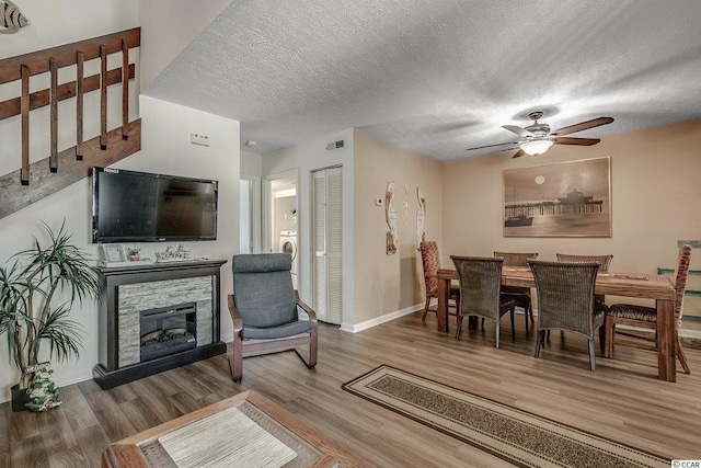 dining room featuring ceiling fan, a textured ceiling, a stone fireplace, and wood-type flooring