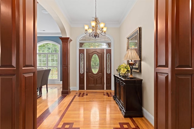 foyer entrance featuring crown molding, decorative columns, a chandelier, and light wood-type flooring